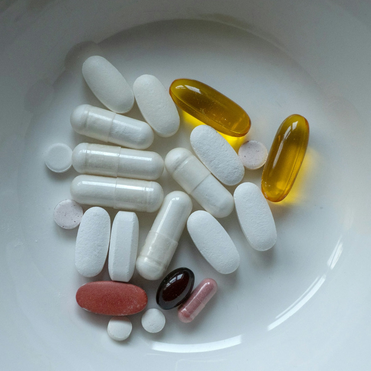 Pills and capsules are inside a white bowl.