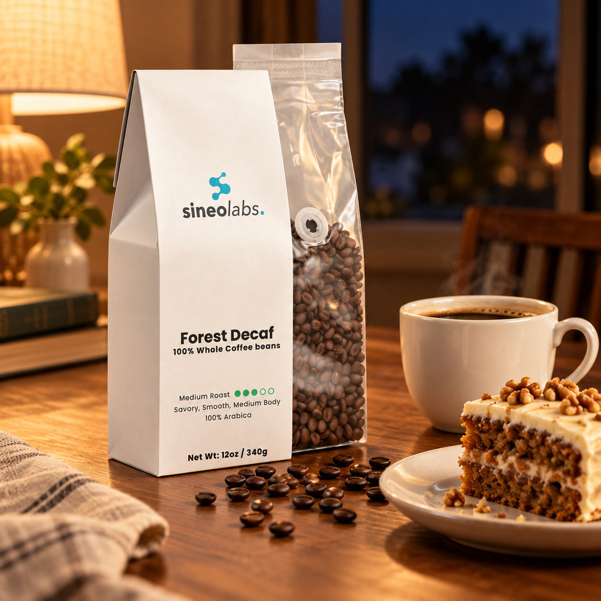 Forest Decaf Swiss Water Coffee, Whole Bean 12oz on a dining table in warm lamp light beside a white cup of coffee and a small plate of cake