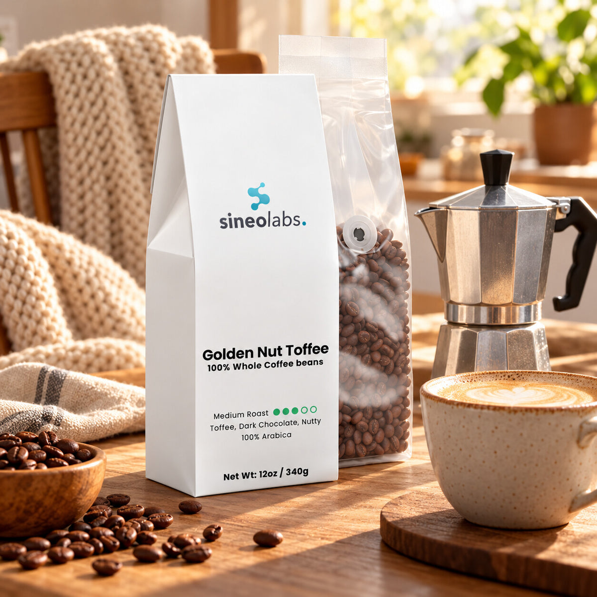 Golden Nut Toffee Medium Roast Coffee, Whole Bean on a cozy kitchen table beside a moka pot and a cup of creamy latte with a little foam