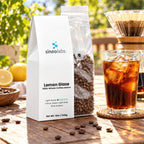 Lemon Glaze Light Roast Coffee, Whole Bean 12oz on a sunny outdoor table beside a tall glass of iced coffee with clear ice and a glass pour-over dripper