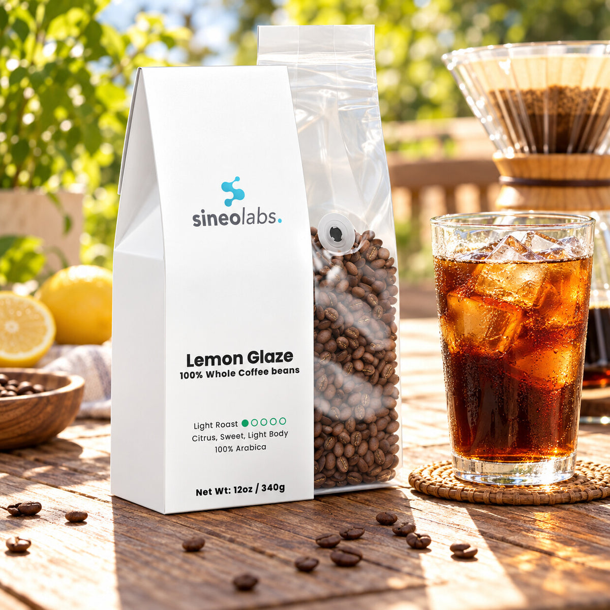 Lemon Glaze Light Roast Coffee, Whole Bean 12oz on a sunny outdoor table beside a tall glass of iced coffee with clear ice and a glass pour-over dripper